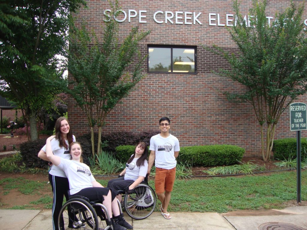 Four dancers, two in wheel chairs, pose outside of Sope Creek Elementary School