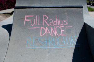 The words Full Radius Dance Restructure are written in pink and blue on the grey concrete of a skatepark ramp.