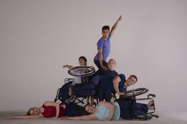 Dancers from the year 2012 create the shape of mountain with their bodies and wheelchairs. Some dancers are parallel to the floor; others are vertical
